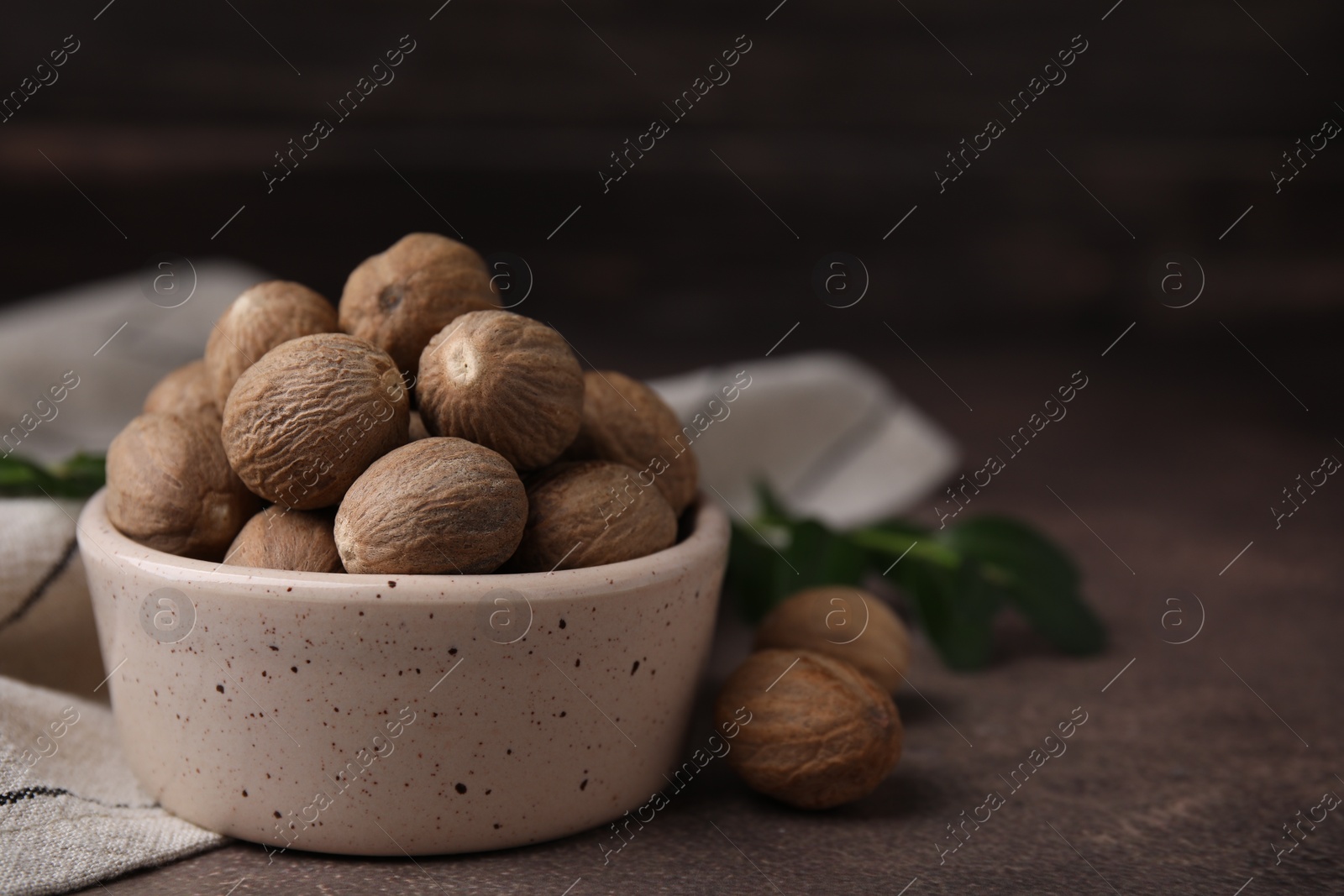 Photo of Whole nutmegs in bowl on brown table. Space for text