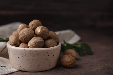 Photo of Whole nutmegs in bowl on brown table. Space for text