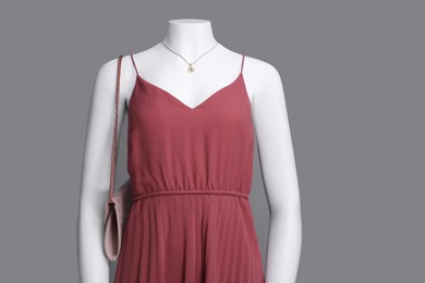 Female mannequin with necklace and bag dressed in stylish red dress on grey background