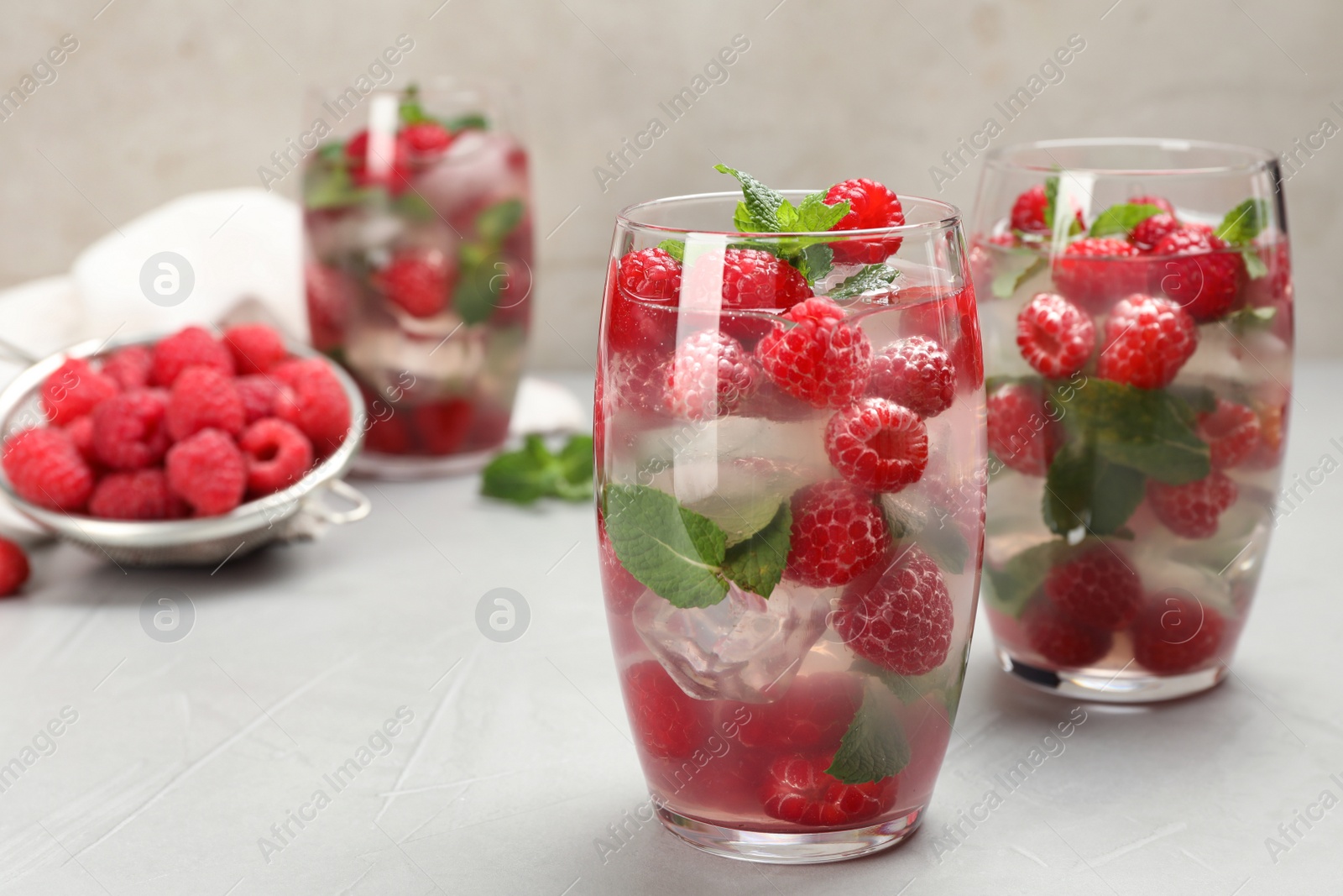 Photo of Glasses of refreshing drink with raspberry and mint on grey stone table, space for text