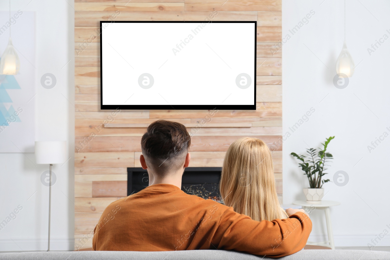 Photo of Couple watching TV on sofa in living room with decorative fireplace