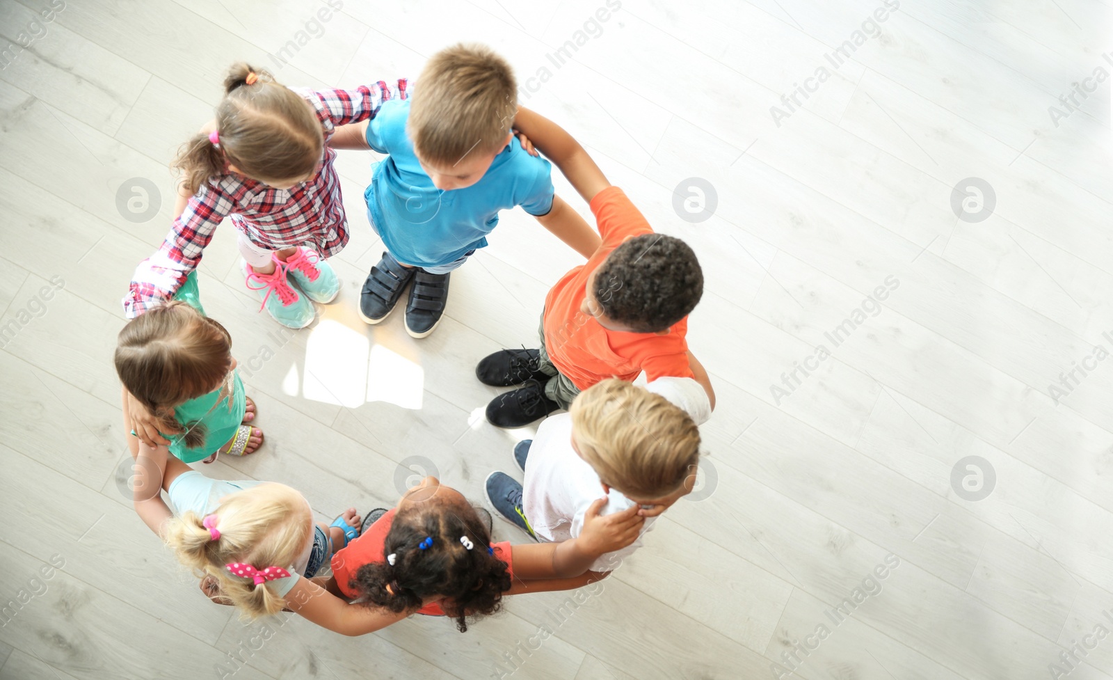 Photo of Little children making circle with hands around each other indoors, top view. Unity concept