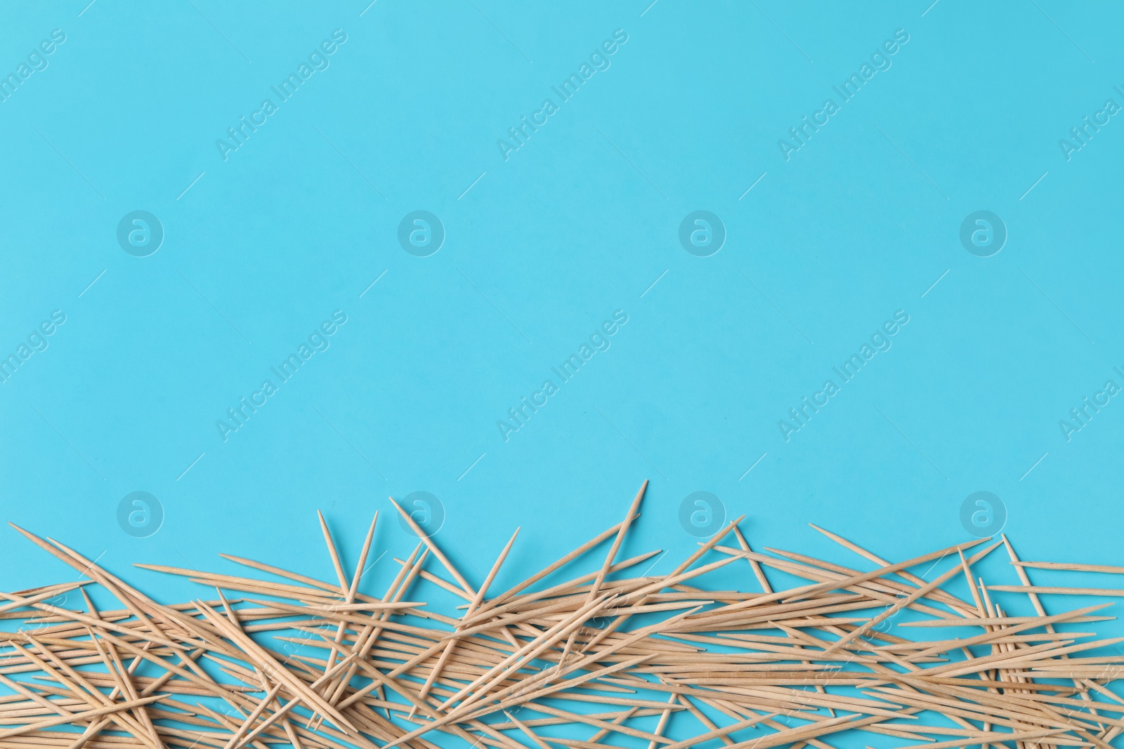 Photo of Wooden toothpicks on light blue background, flat lay. Space for text