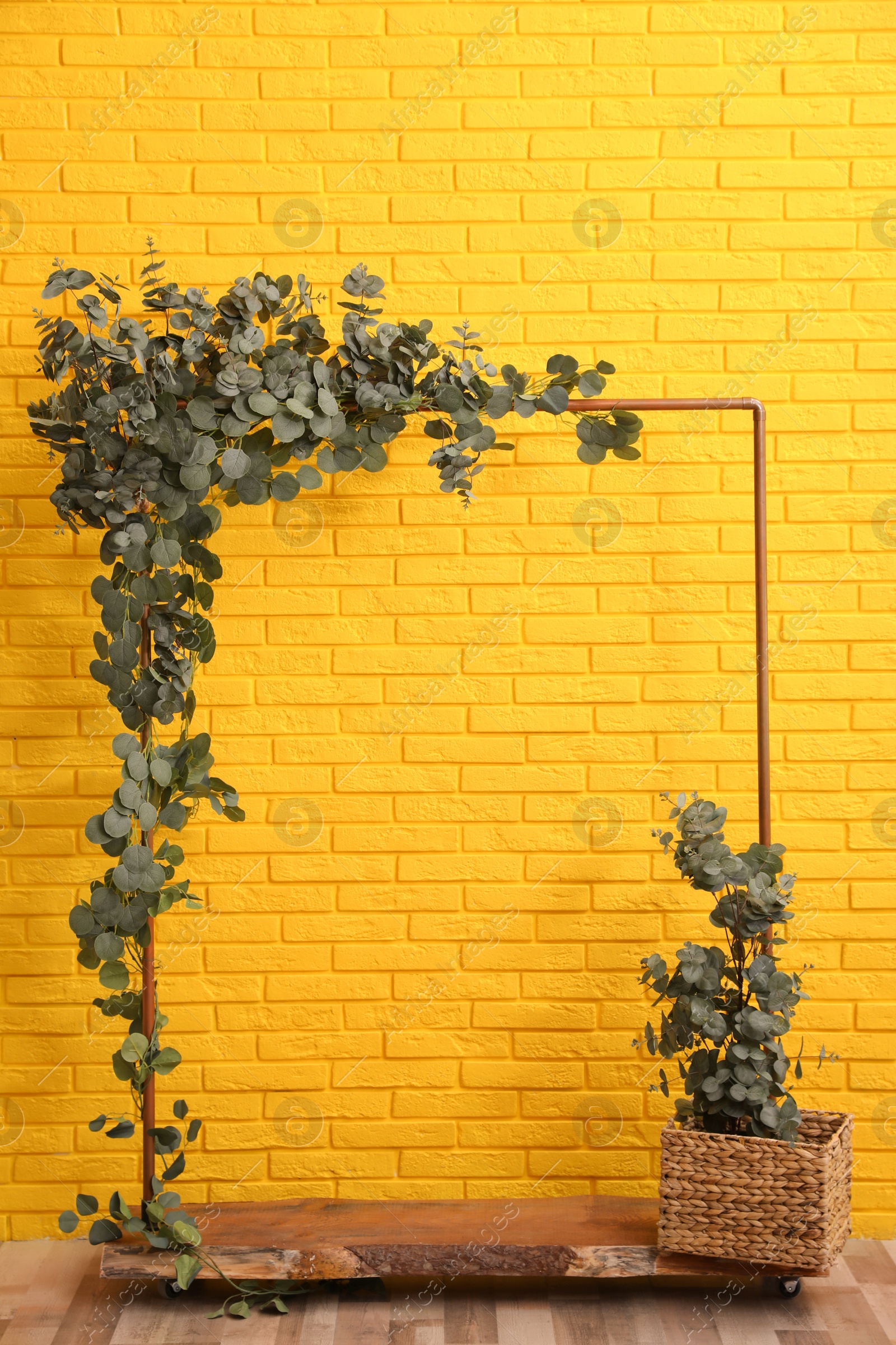 Photo of Stylish photo zone with wooden frame and green leaves near yellow brick wall indoors