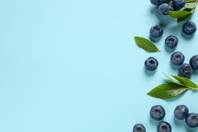 Tasty fresh blueberries with green leaves on light blue background, flat lay. Space for text
