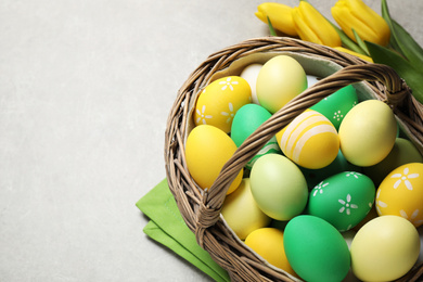 Photo of Many Easter eggs in wicker basket and yellow tulips on grey background