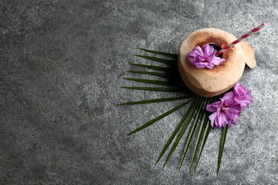 Photo of Young peeled coconut with straw, palm leaf and flowers on grey table, flat lay. Space for text