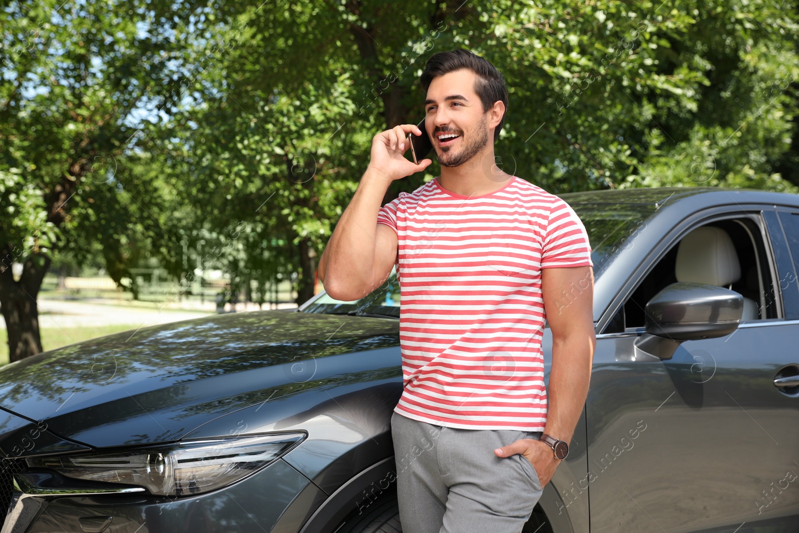 Photo of Attractive young man talking on phone near luxury car outdoors