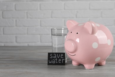 Card with phrase Save Water. Piggy bank and glass of drink on wooden table, space for text