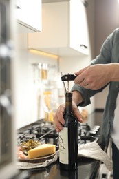 Man opening wine bottle with corkscrew at black countertop indoors, closeup