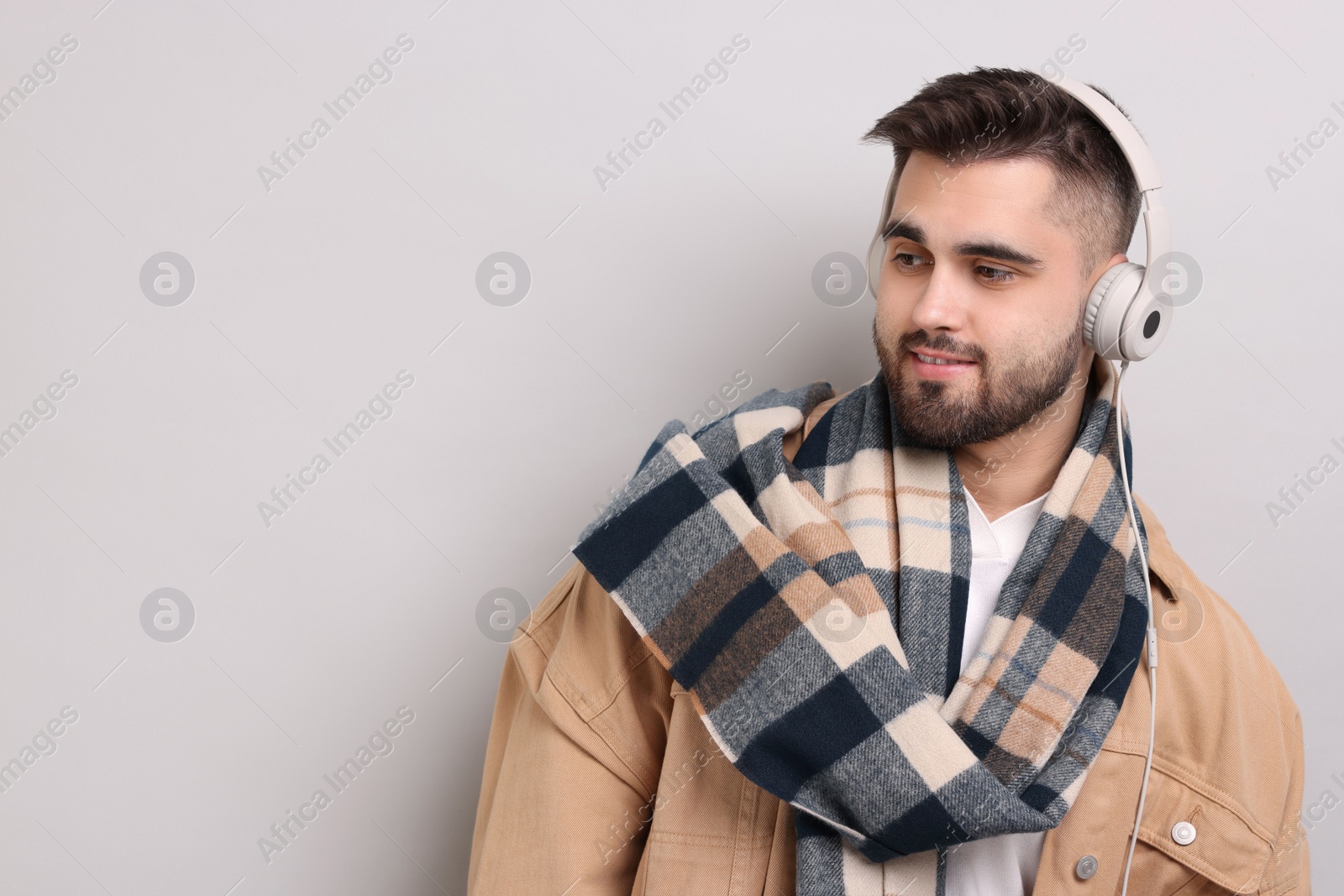 Photo of Smiling man in warm scarf listening to music on light grey background. Space for text