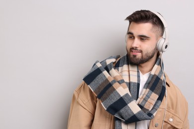 Smiling man in warm scarf listening to music on light grey background. Space for text