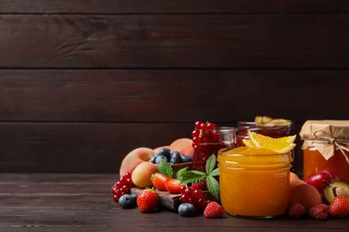 Jars with different jams and fresh fruits on wooden table. Space for text