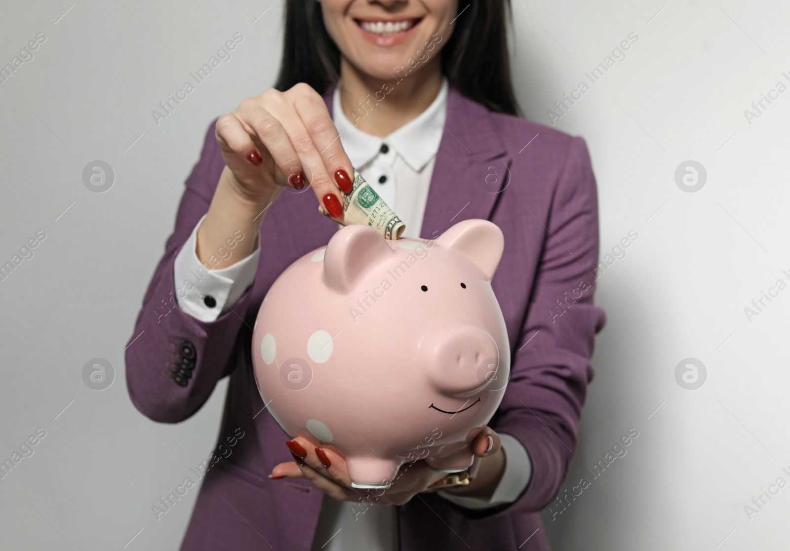 Photo of Businesswoman putting money into piggy bank on light background, closeup