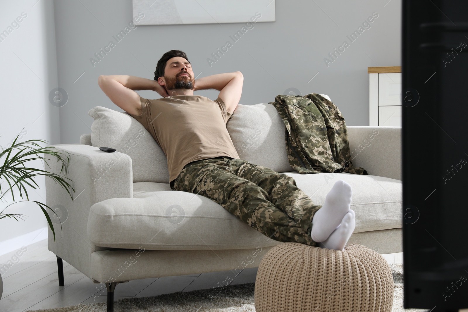 Photo of Soldier napping on soft sofa near TV in living room. Military service