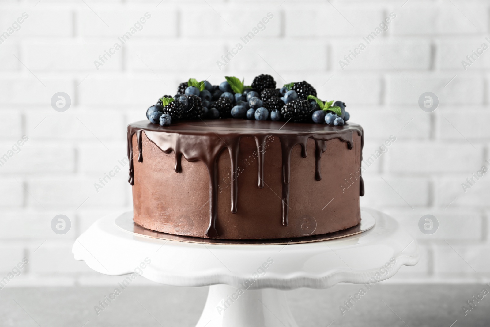 Photo of Fresh delicious homemade chocolate cake with berries on table against brick wall