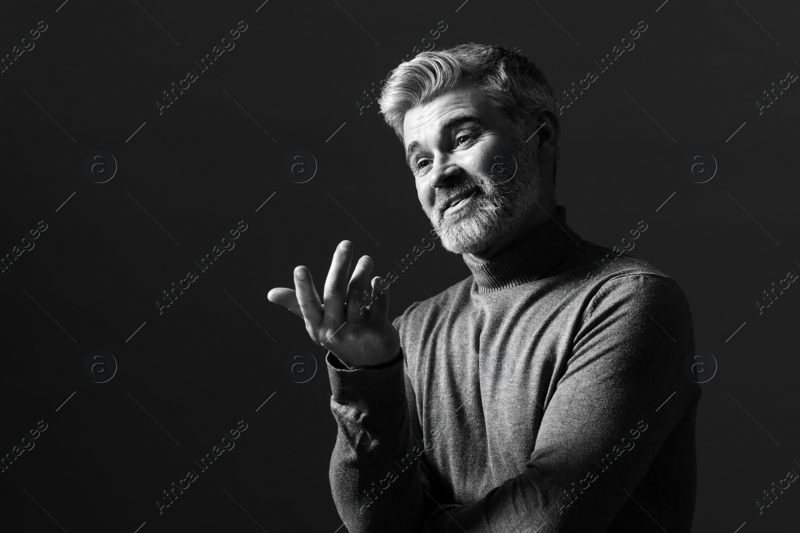 Photo of Portrait of smiling man gesturing on dark background. Black and white effect