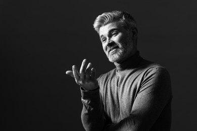 Portrait of smiling man gesturing on dark background. Black and white effect