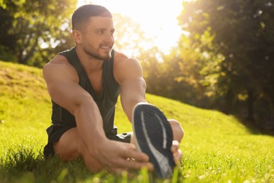 Attractive man doing exercises on green grass in park, space for text. Stretching outdoors