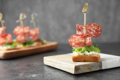 Photo of Tasty canapes with salami, greens and cream cheese on grey table, closeup. Space for text