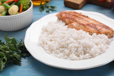 Photo of Grilled chicken breast and rice served with vegetables on light blue wooden table, closeup