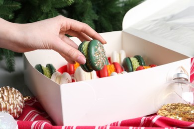 Woman with box of decorated Christmas macarons at table, closeup