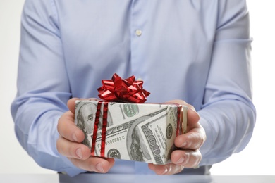 Man holding gift box wrapped in decorative paper with dollar pattern on white background, closeup