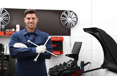 Photo of Professional worker with wheel wrench in shop of modern tire service