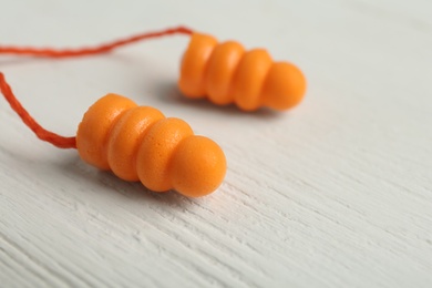 Pair of orange ear plugs with cord on white wooden background, closeup. Space for text