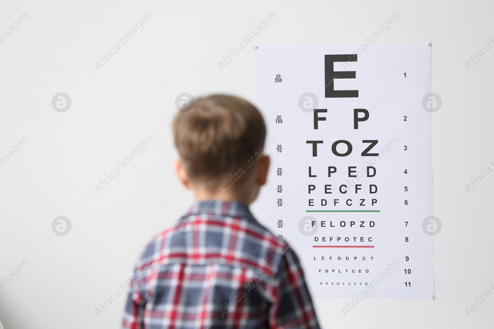 Photo of Eyesight examination. Little boy looking at vision test chart indoors, back view