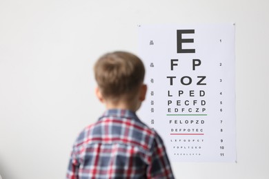 Photo of Eyesight examination. Little boy looking at vision test chart indoors, back view