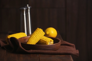 Photo of Plate with ripe corn cobs on table against dark background