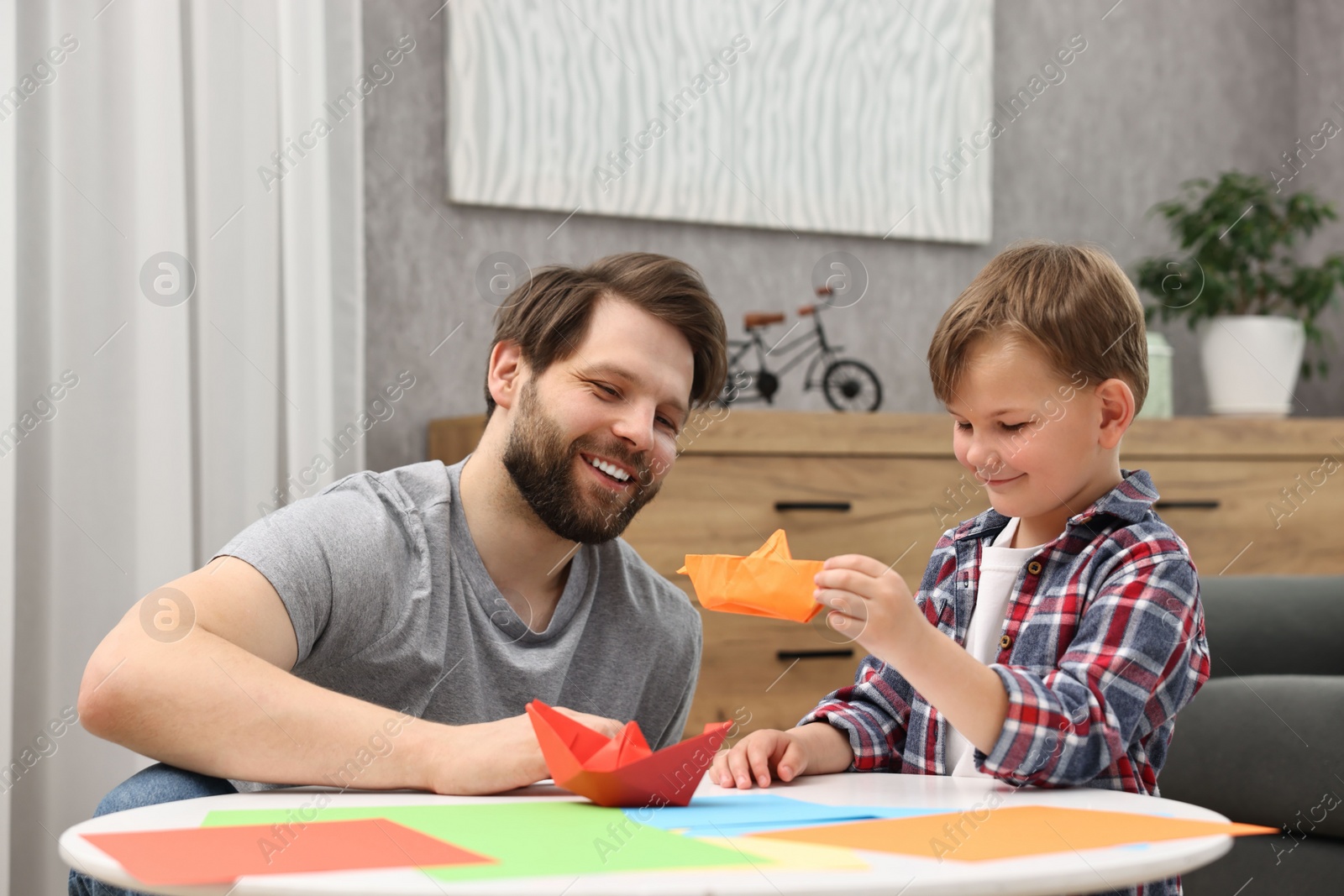 Photo of Dad and son making paper boats at coffee table indoors