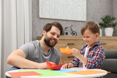 Photo of Dad and son making paper boats at coffee table indoors