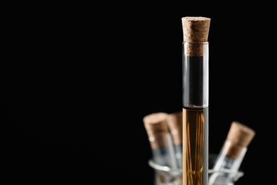 Test tube with brown liquid on black background, closeup. Space for text