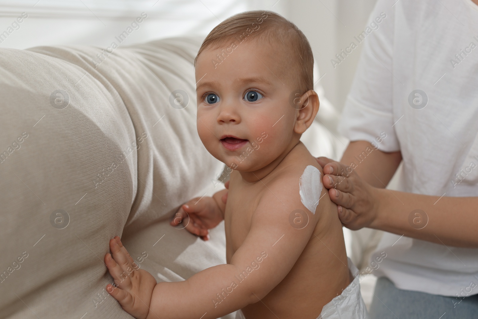 Photo of Mother applying body cream on her little baby at home, closeup