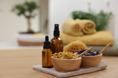 Bottles of essential oils, bowls with dry flowers and natural sponge on light wooden table, space for text. Spa therapy