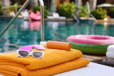 Photo of Beach towels, sunglasses and sunscreen on sun lounger near outdoor swimming pool at luxury resort
