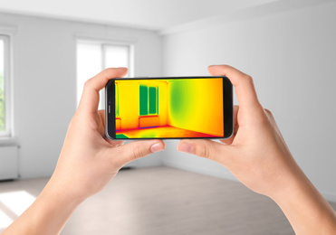 Image of Woman detecting heat loss in room using thermal viewer on smartphone. Energy efficiency