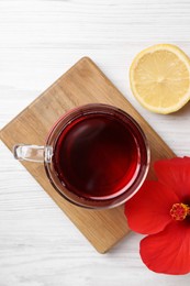 Delicious hibiscus tea, lemon and beautiful flower on white wooden table, flat lay