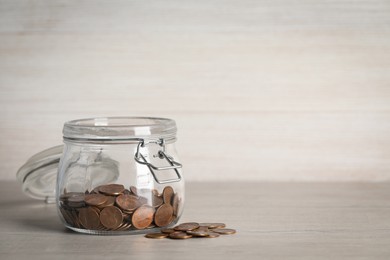 Photo of Glass jar with coins on white wooden table. Space for text