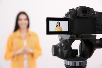 Young blogger recording video against white background, focus on camera screen