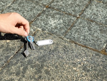 Photo of Woman picking bunch of keys from pavement outdoors, closeup. Space for text