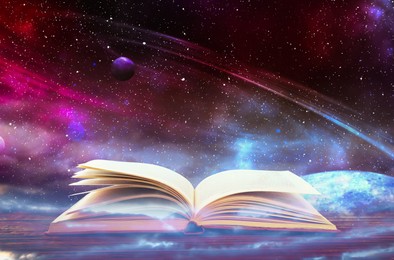 Image of Wooden table with open book and beautiful universe on background