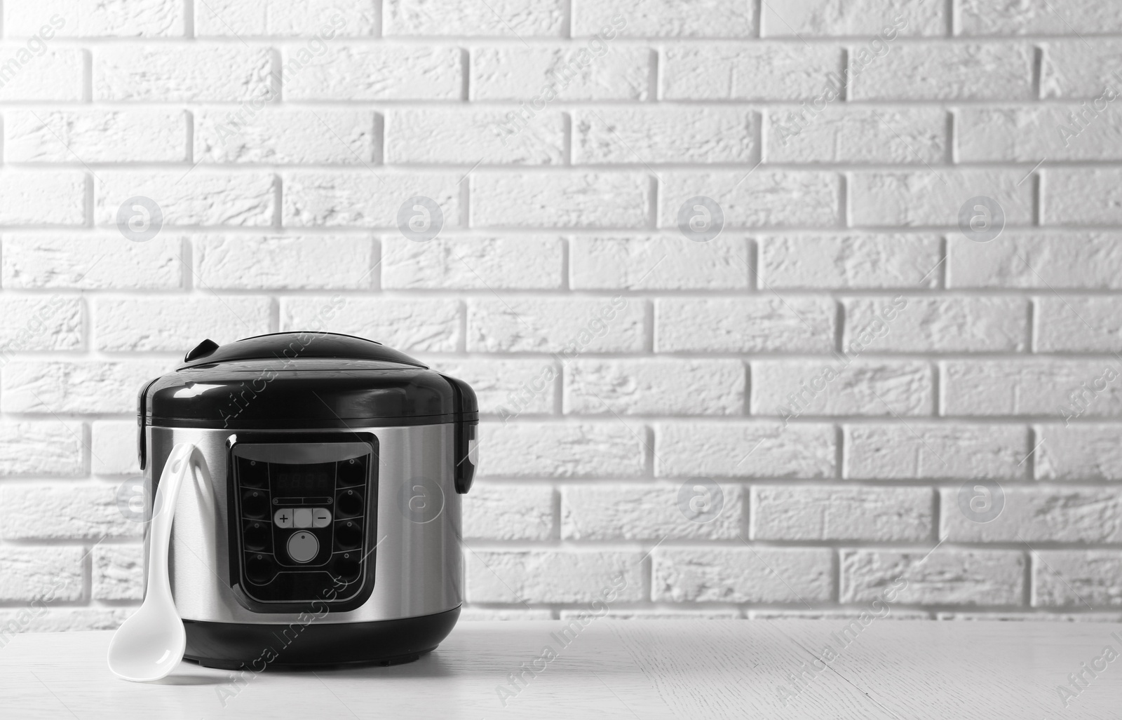 Photo of Modern multi cooker on table against brick wall. Space for text