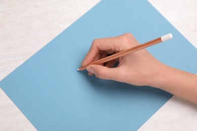Photo of Woman drawing on light blue paper with pastel pencil at white wooden table, top view