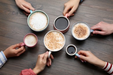 Photo of People holding different cups with aromatic hot coffee at wooden table, top view