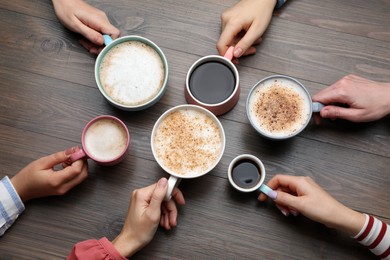 People holding different cups with aromatic hot coffee at wooden table, top view