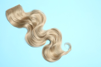 Lock of blonde wavy hair on color background, top view. Space for text