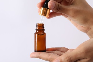 Woman with bottle of cosmetic serum and dropper on white background, closeup
